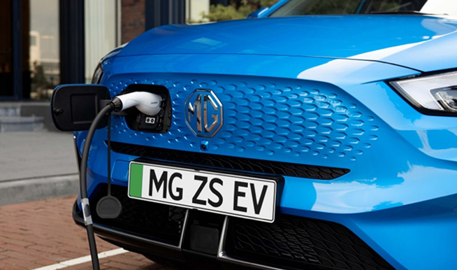 Closeup image of the front charging port, badge, and grille of a blue MG ZS EV.