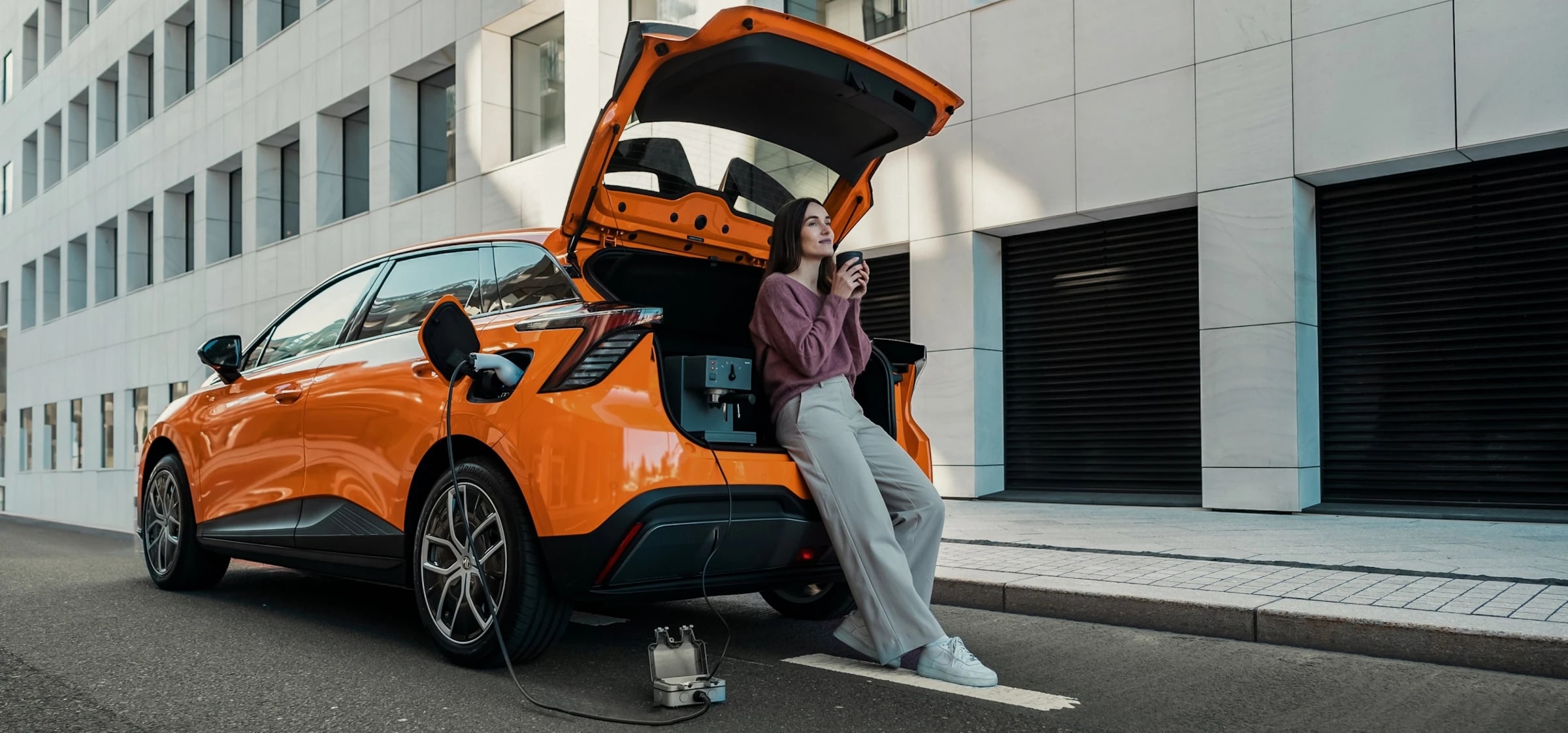Image of woman leaning against the open boot of an orange MG 4 EV